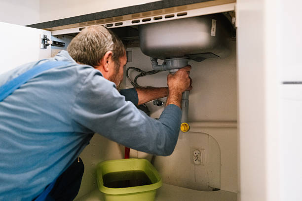 From above of crop anonymous person in yellow rubber protective glove using sponge and detergent for washing white sink in bathroom